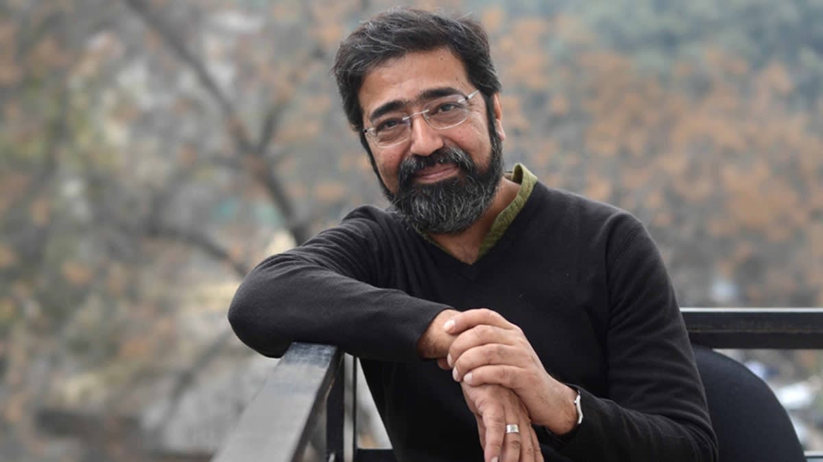 A portrait of an Indian man with glasses in a black sweater.