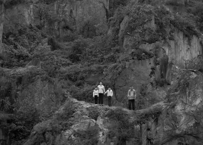 Black and white wide-angle photograph of a man, a woman and two children against a dense forest background. 