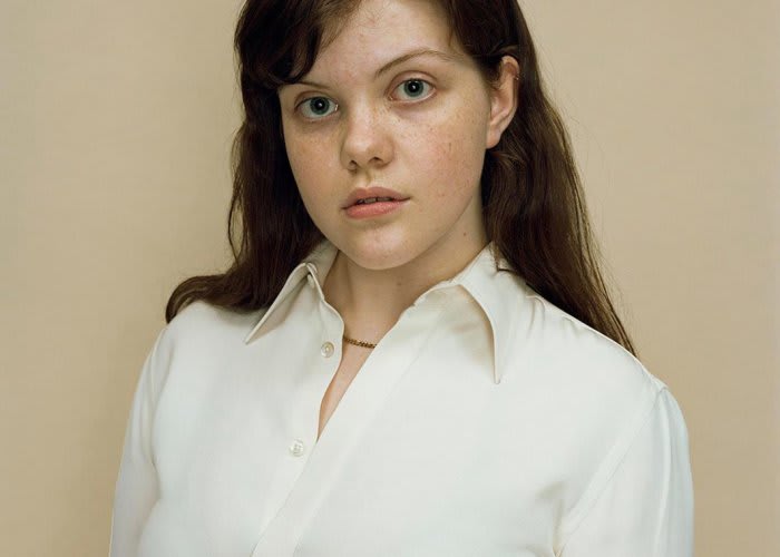 A close up portrait of a young brunette woman wearing a white blouse.
