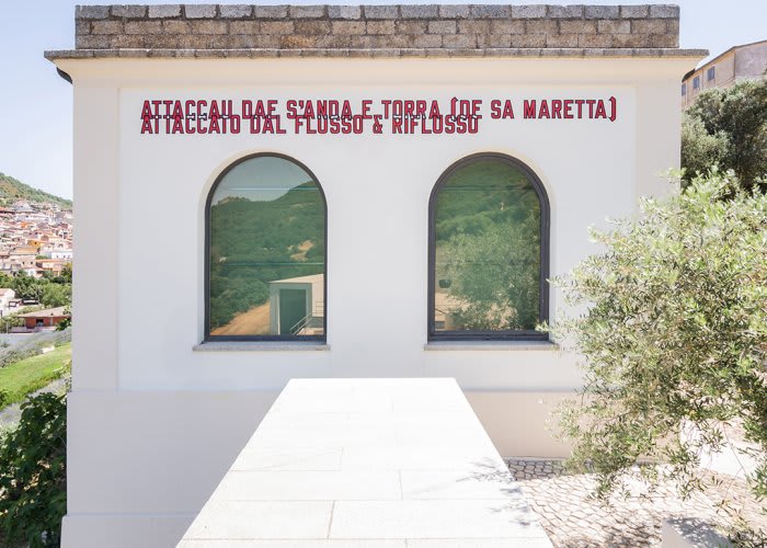 Outdoor image of wall with arched windows and red text above.