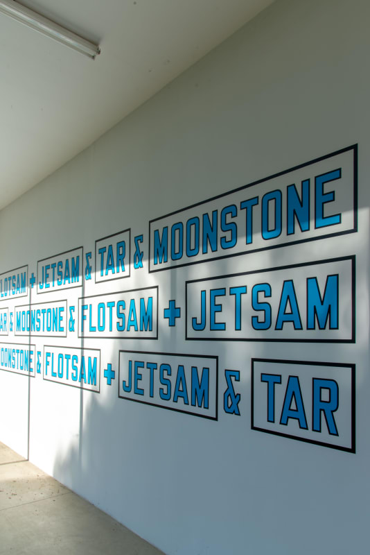 Installation view of a work by Lawrence Weiner at Venet Foundation in France; The statement reads, as follows, in both English and French: ⠀ ⠀ Flotsam + Jetsam + Tar + Moonstone ⠀ Tar + Moonstone + Flotsam + Jetsam⠀ Moonstone + Flotsam + Jetsam + Tar⠀ ⠀ D