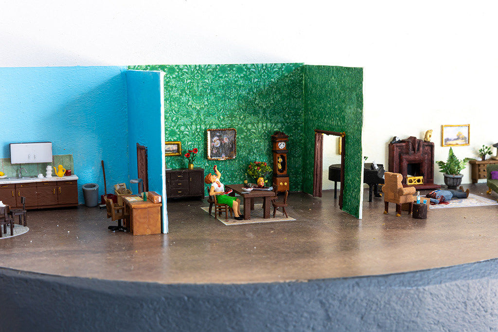 miniature diorama by Abigail Goldman of a house interior with a woman sitting at a dining table with a severed head