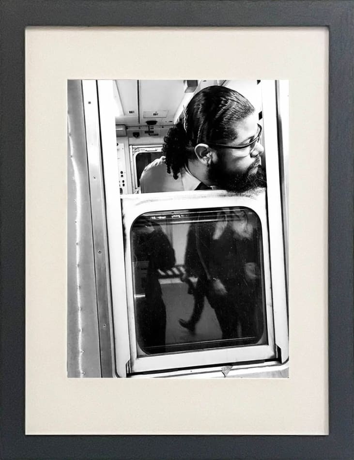 black and white photo of subway train conductor looking out the window in black frame