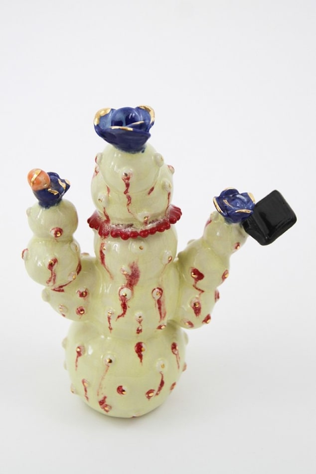 Jen Dwyer sculpture - beige cactus with red accents and one eyeball at center, holding black laptop and other accessories