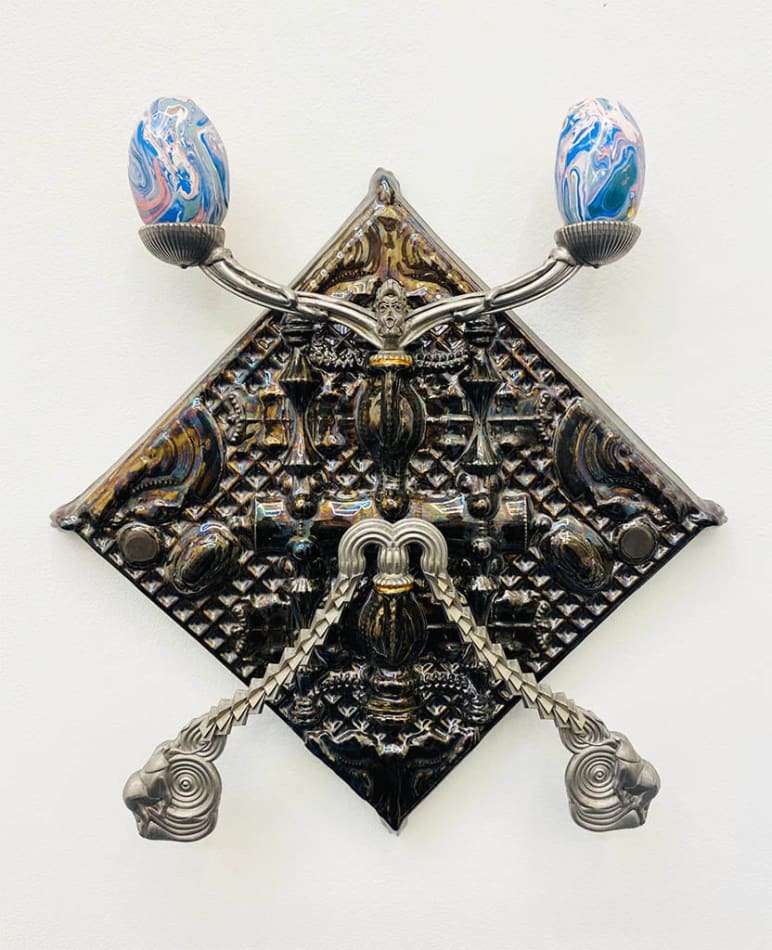 silver candelabra hung on a white wall holding two multicolored eggs