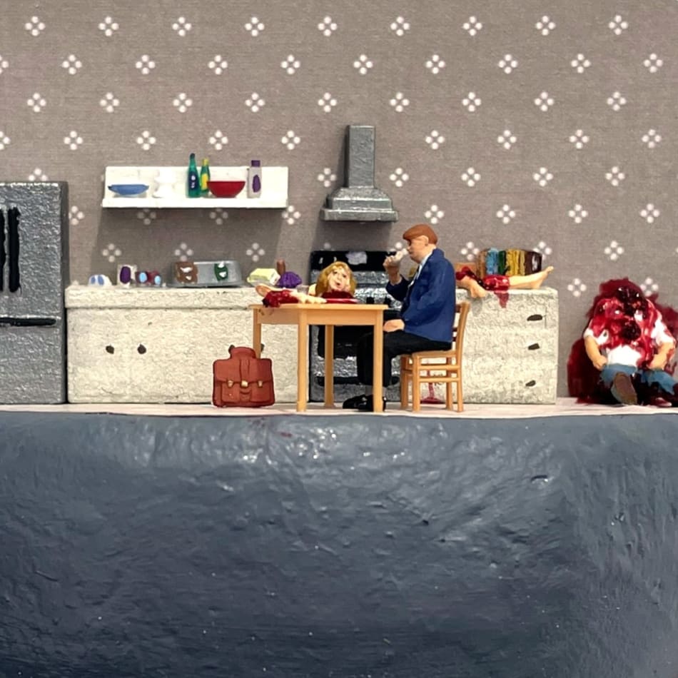 man sitting at kitchen table with a decapitated head in front of him