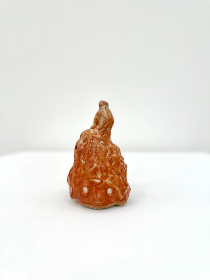Ceramic sculpture of a head with a pointy top in a burnt orange glaze.