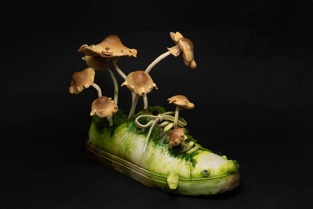Sculpture of a shoe covered with moss with mushrooms with dog faces growing out of it