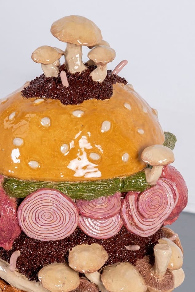 Detail of Lindsey Lou Howard sculpture of giant burger with onions, tomatoes, mushrooms, all in excessive amounts