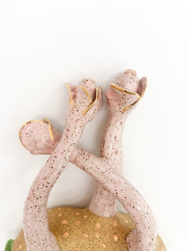 detail shot of sculpture by Jen Dwyer of light pink tentacle like objects emerging from brown mound with green leafs
