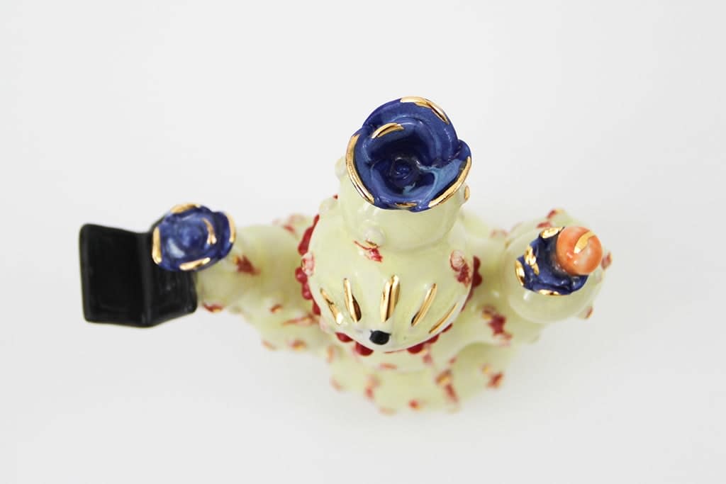 Jen Dwyer sculpture - beige cactus with red accents and one eyeball at center, holding black laptop and other accessories