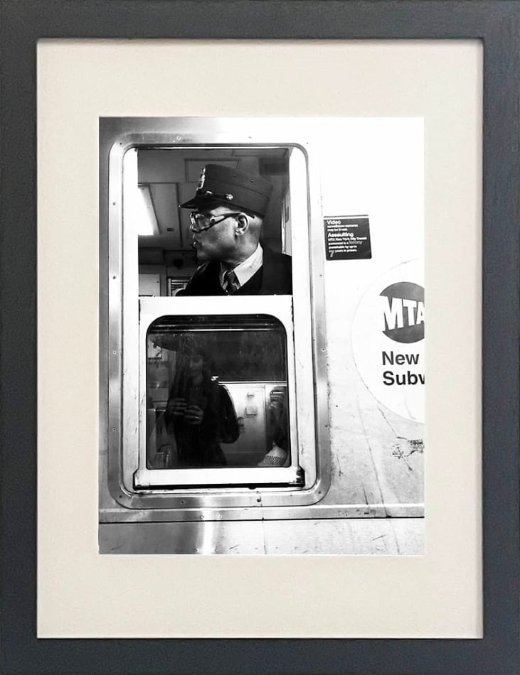 black and white photo of subway train conductor looking out window in black frame