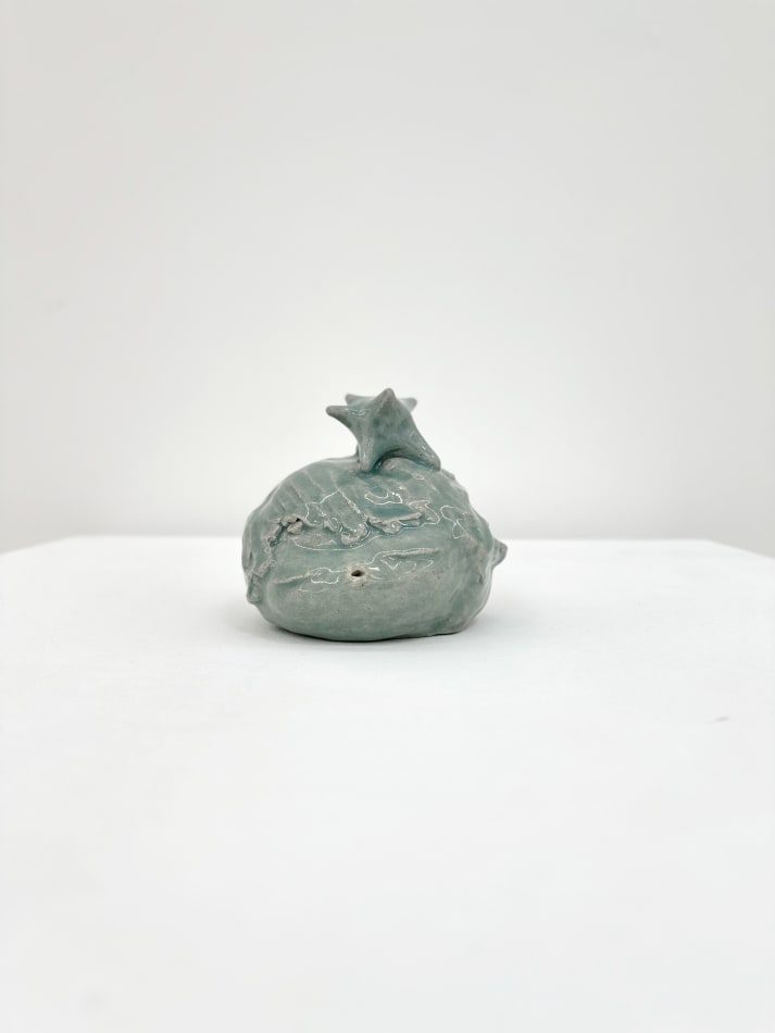 Ceramic sculpture of a head with its eyes closed and a star on top of its head in a light green glaze