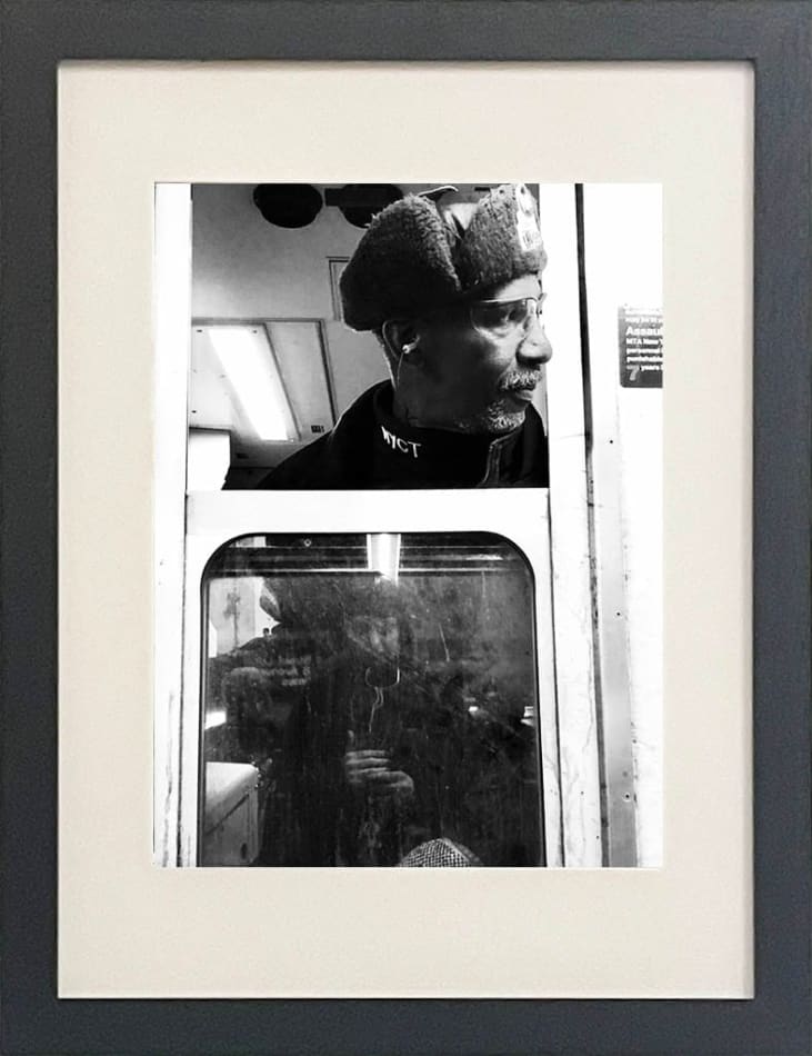 black and white photo of subway train conductor looking out the window in black frame