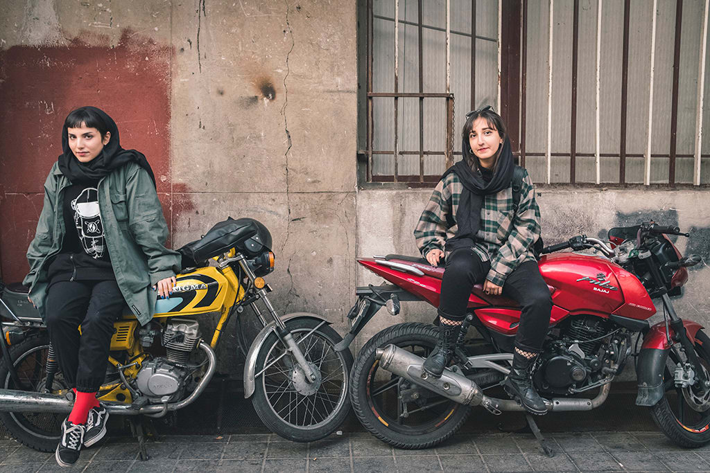 Photo of two women sitting on red and yellow motorcycles