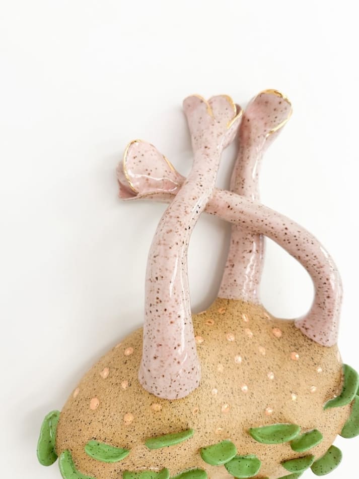 detail shot of sculpture by Jen Dwyer of light pink tentacle like objects emerging from brown mound with green leafs