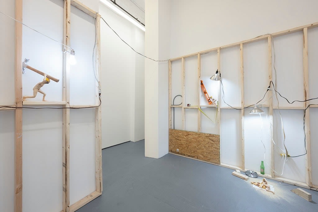 view of entrance to room with white walls, wooden scaffolding, and various dog human sculptures displayed in various scenes