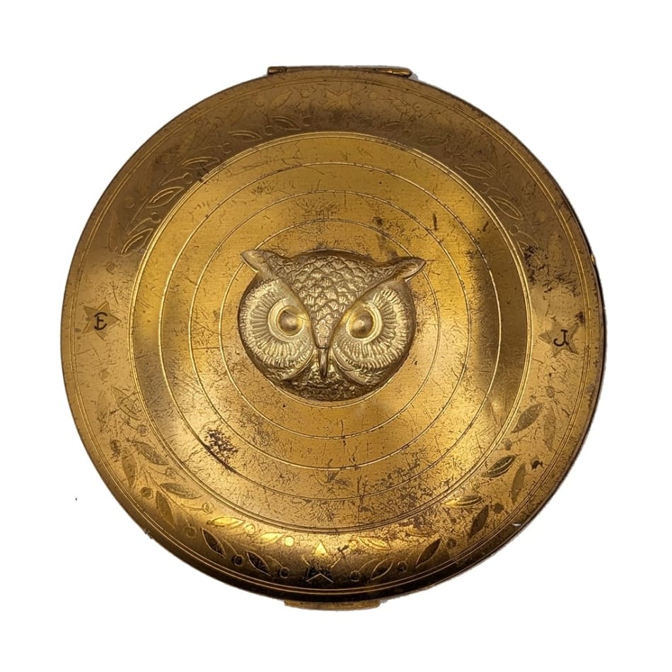 gold cosmetic compact with gold owl face in the center