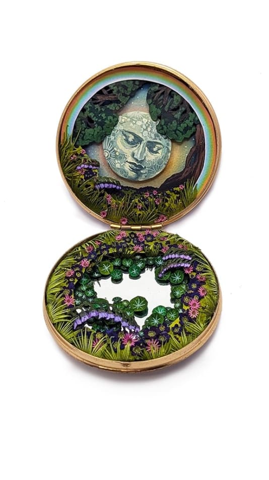hand-cut watercolor collage in antique cosmetic compact by Shannon Taylor of a large moon with a face and tons of flowers and leaves surrounding it