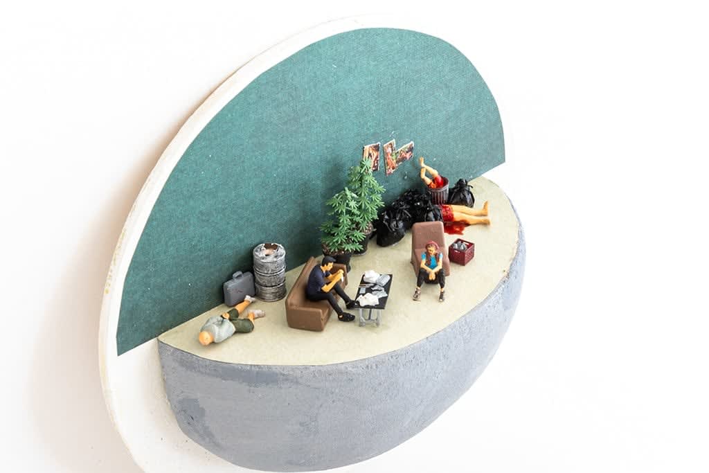 miniature diorama by Abigail Goldman of two people sitting around a table covered in paper and dead bodies in the background