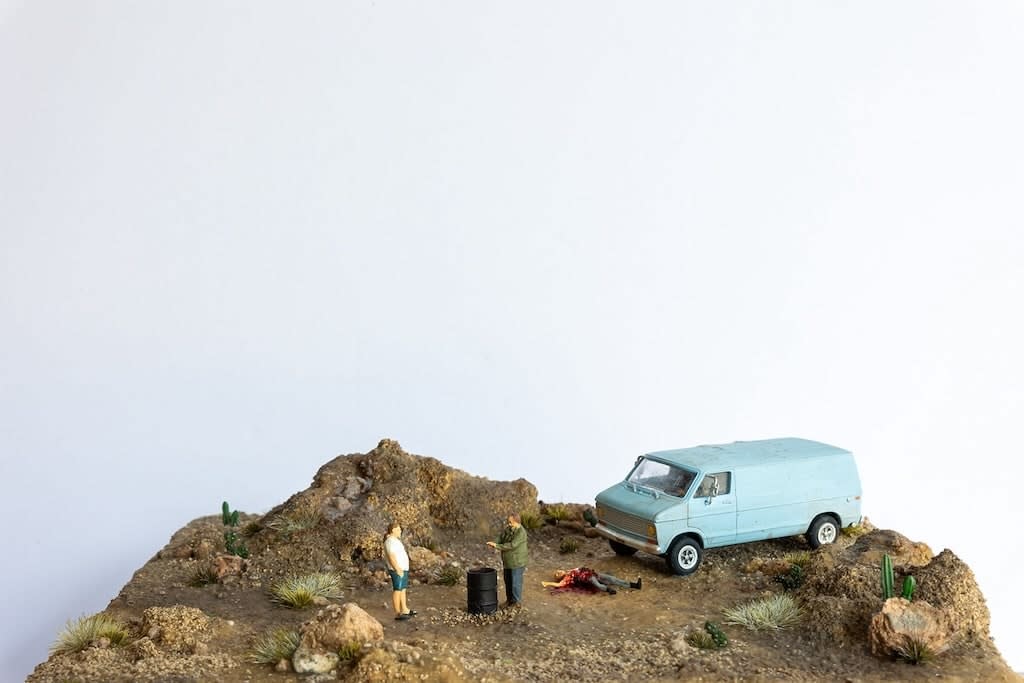 miniature diorama by Abigail Goldman of two man standing next to a burn barrel and a dead body on the dessert