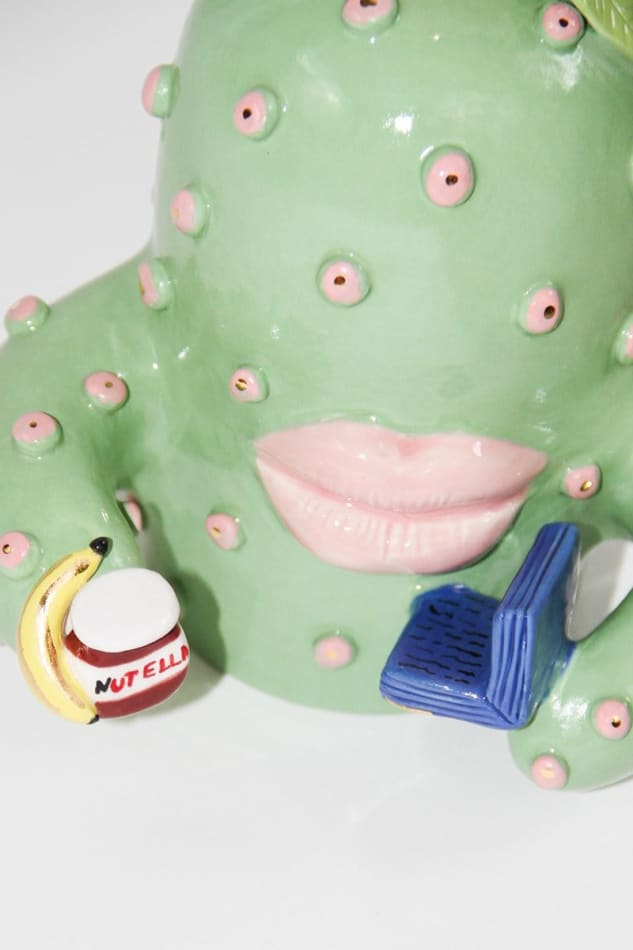 detail od Jen Dwyer sculpture of green cactus with pink lips holding laptop, banana and Nutella jar
