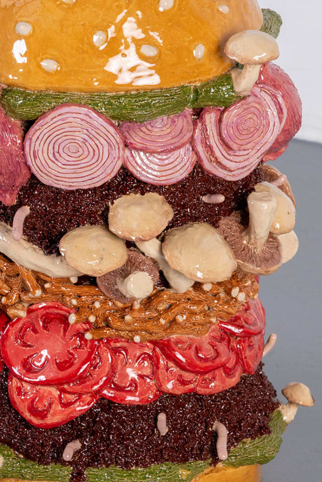 Detail of Lindsey Lou Howard sculpture of giant burger with onions, tomatoes, mushrooms, all in excessive amounts