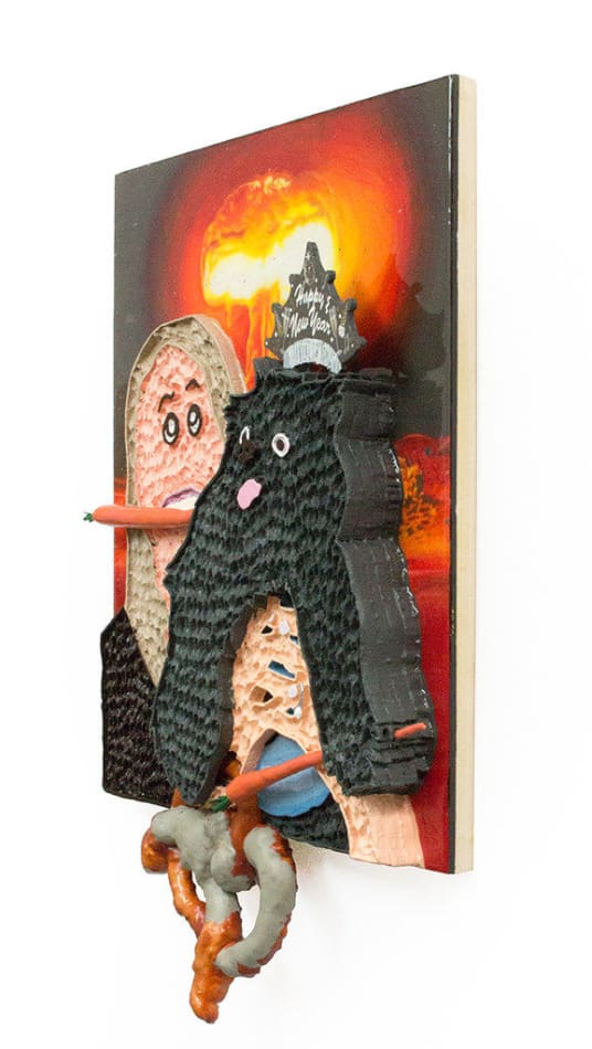 Mixed media hanging sculpture of a woman with a carrot in her mouth holding a small black dog with a Happy New Year paper crown on his head and a pretzel and a carrot in his hands. In the background an atomic bomb is going off.