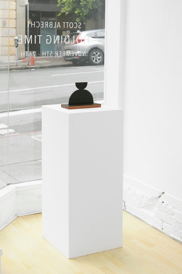 Scott Albrecht steel sculpture - two semi circles, larger one balanced on smaller one. Wood base - side view