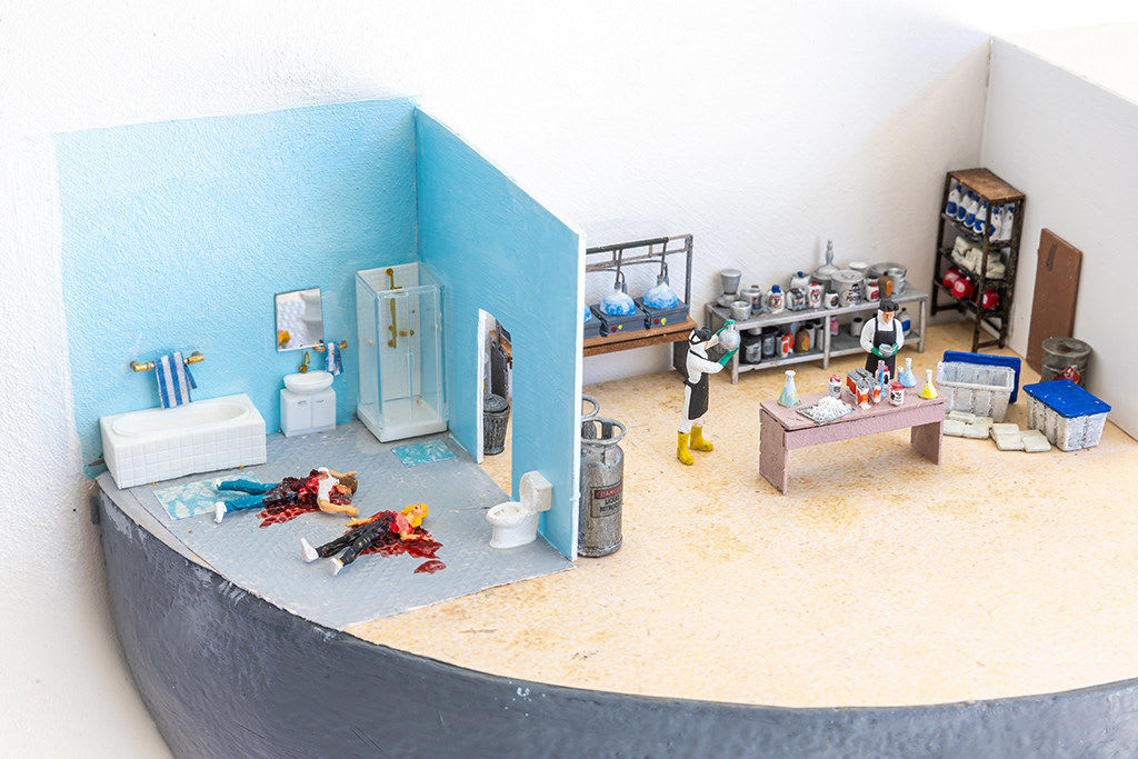 miniature diorama by Abigail Goldman depicting three scenes, two people dead in a bathroom, a laboratory and a family watching tv