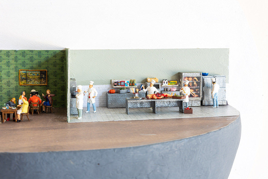 miniature diorama by Abigail Goldman of a restaurant with a human body being prepared in the kitchen s