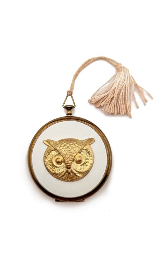 gold round cosmetic case with white middle and a gold owl in the center and a powder pink tassel attached the side