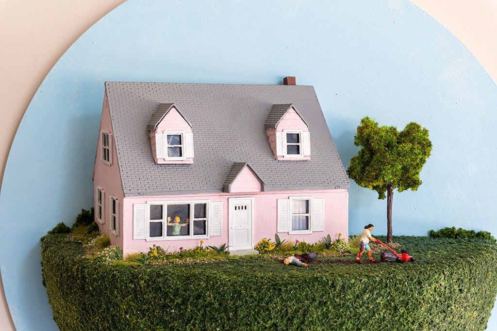 miniature diorama by Abigail Goldman of a woman running over a body with a lawnmower in the front yard of a pink house
