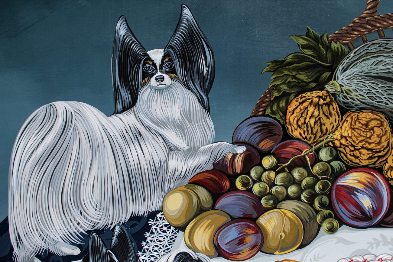 Tablescape painting of two black and white dogs on a table full of decadent food, including a basket of fruit with a grasshopper on it, a giant bouquet of flowers, a bowls of strawberries that has been know knocked over, a plate of giant shrimp, a bowl of whole fish and a white frosted cake that one of the dogs has walked into and gotten frosting all over the table.