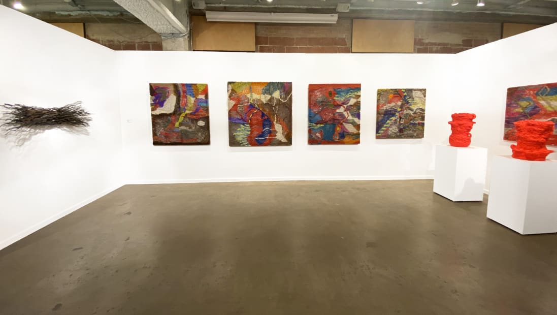Installation view at the Dallas Art Fair with several colorful knitted works by Channing Hansen, red pots on plinths by Beverly Semmes, and a bundle of twisted wire rope on the wall by Maren Hassinger