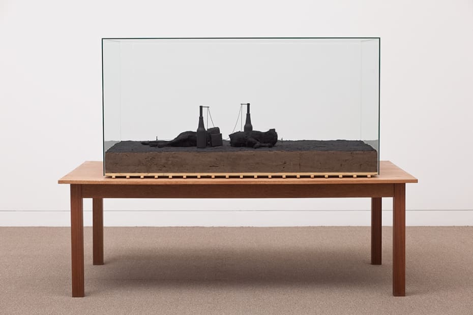 Image of Mark Manders sculpture with dark table and glass case