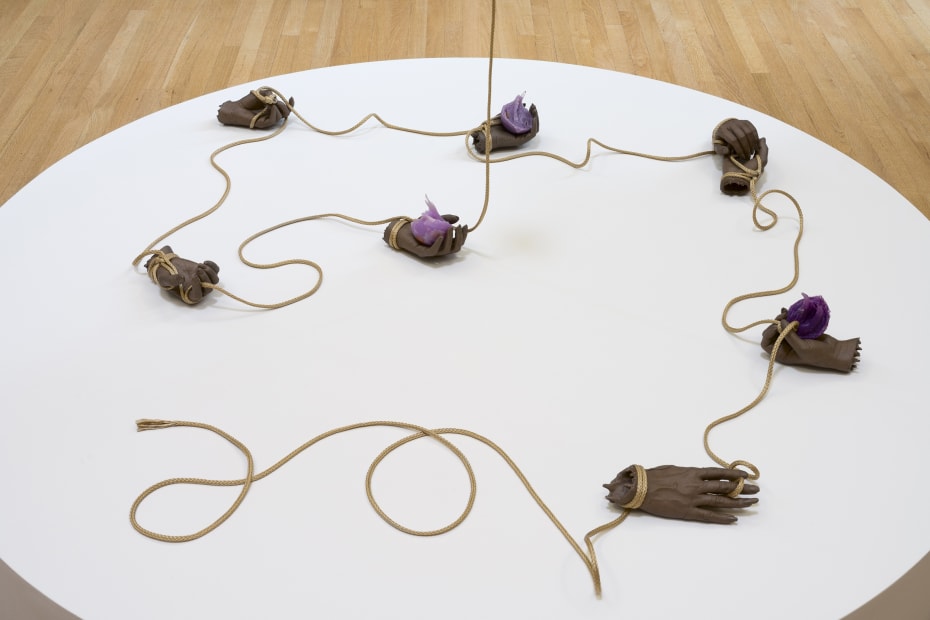earthen hand sculptures connected by tubes, on a circular white pedestal