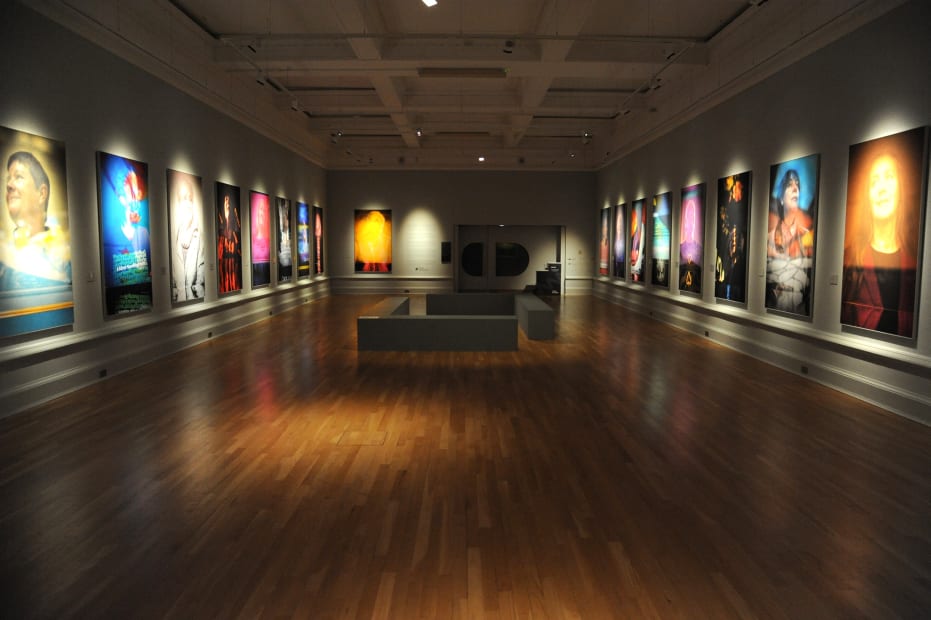 colorful portraits of women hung in a row on two sides of a gallery