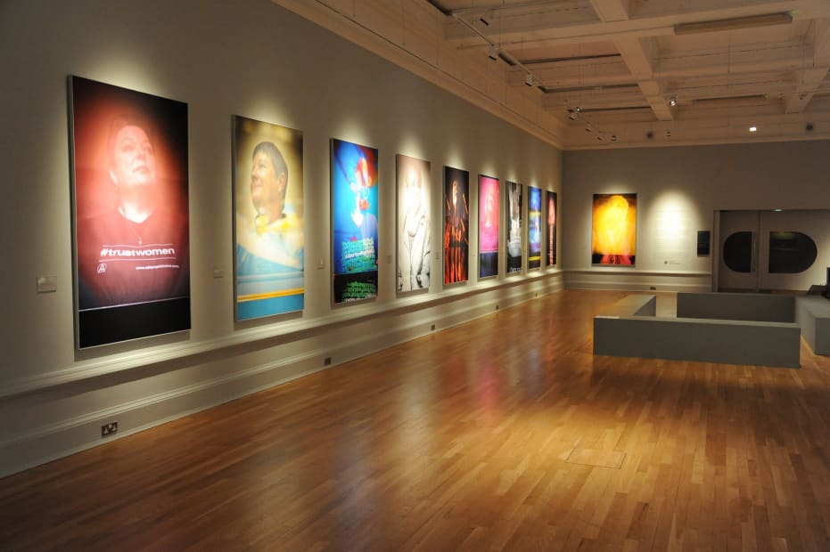colorful portraits of women hung in a row on the left wall of a gallery