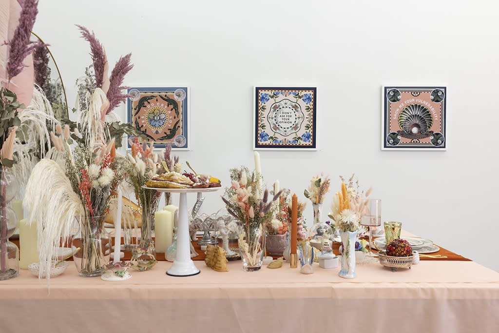 side image of table installation with artwork on wall behind in Marie-Claude Marquis "Inner Romance" show