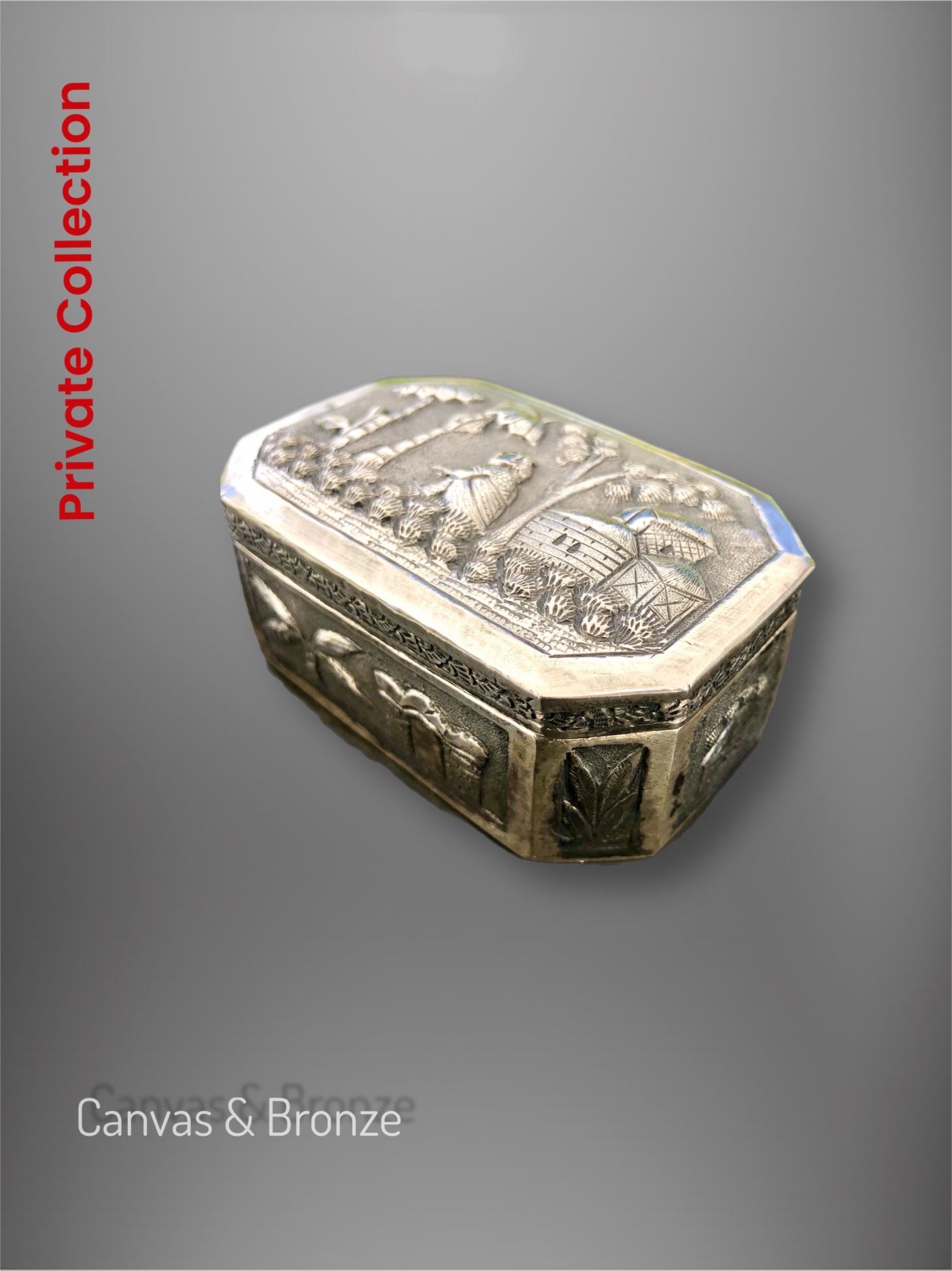 Antique silver box with intricate engravings and embossed cultural motifs, displayed against a gray background.