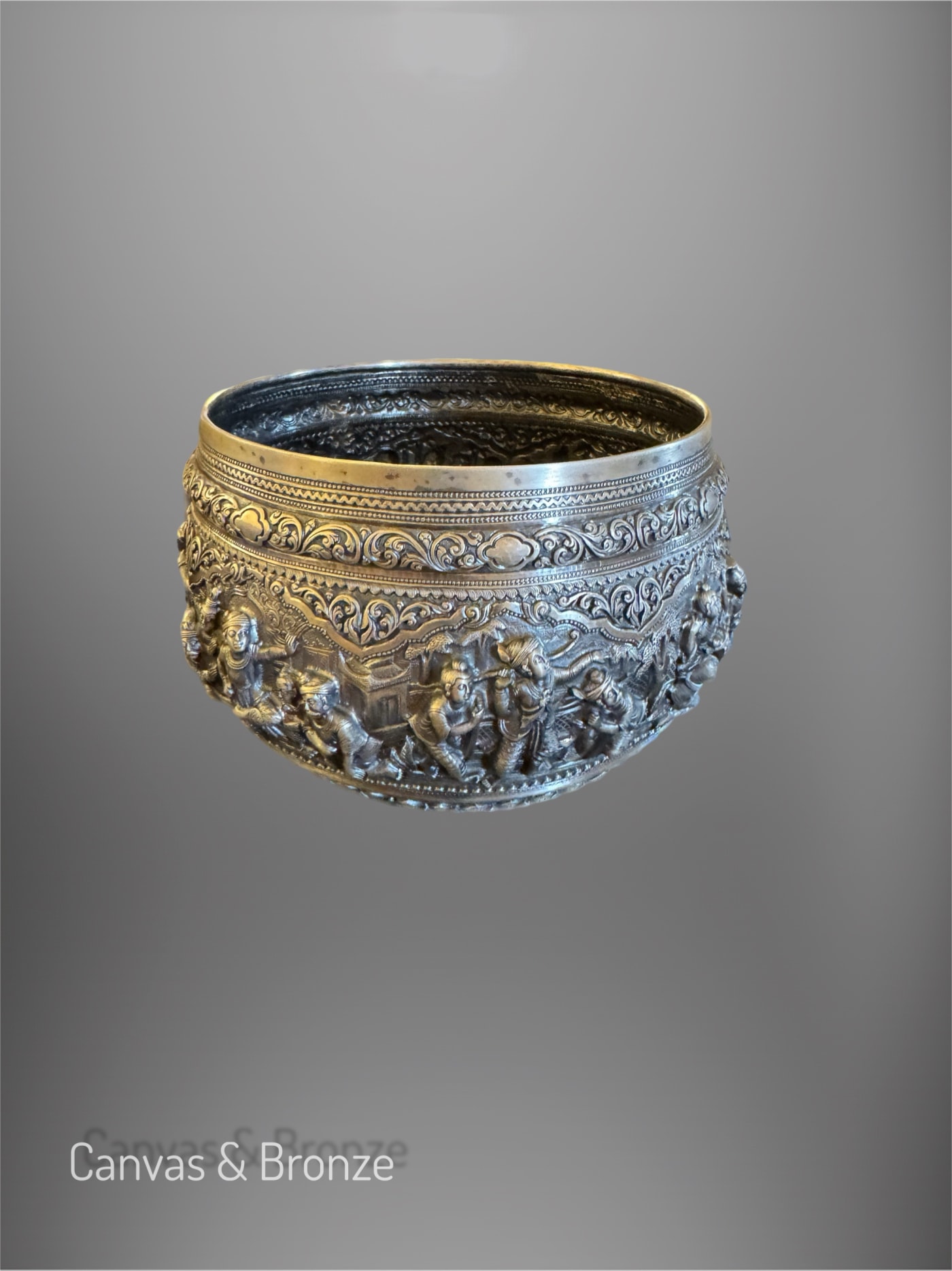 Ornate silver bowl with intricate relief carvings depicting historical and cultural scenes, featuring detailed patterns and figures.