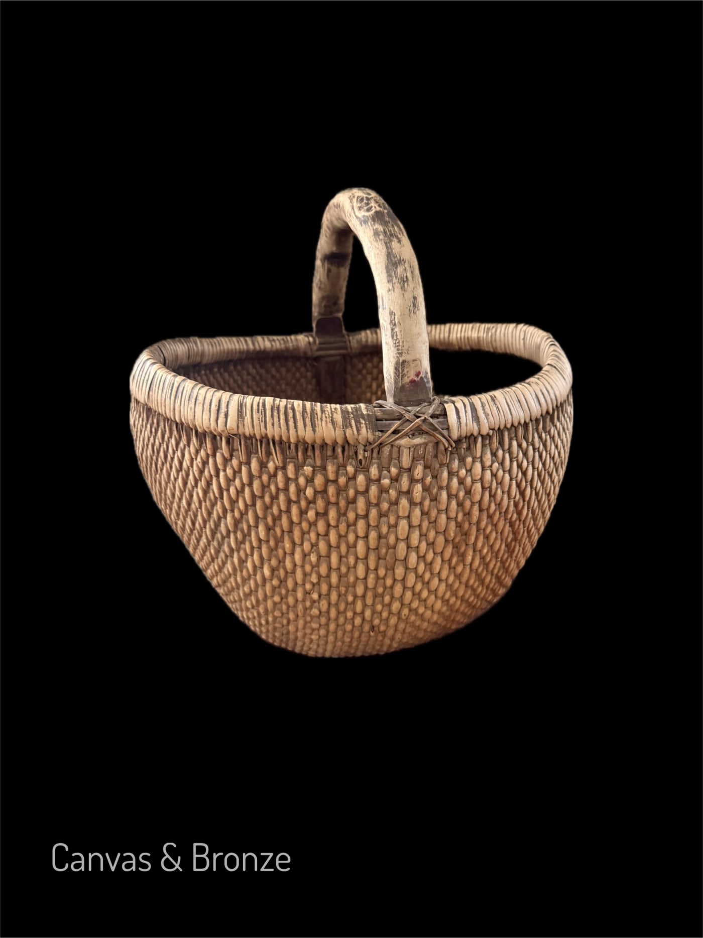 Woven basket with a curved handle on a black background.