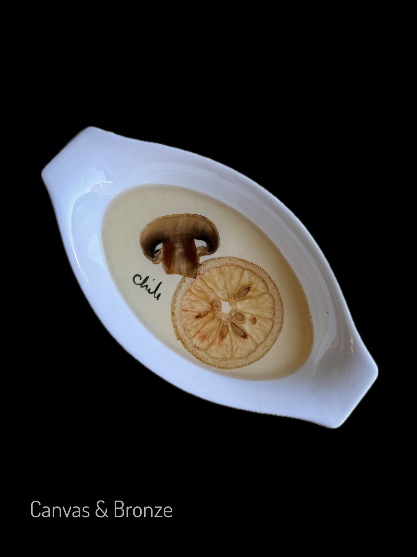 Oval ceramic dish with a mushroom slice and dried citrus, featuring the word "Chile" on a dark background.