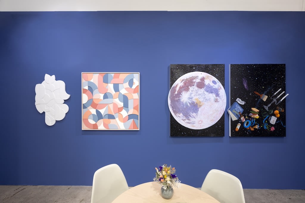 blue booth with various artworks hanging on walls. round table in foreground