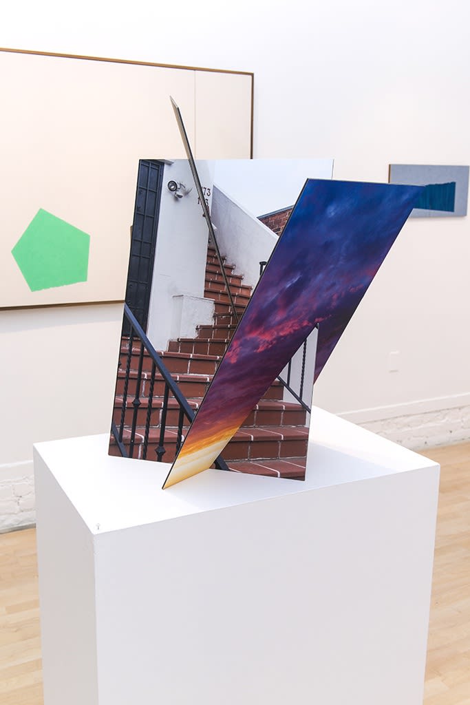 Exhibition installation view featuring abstracted sculptural work in foreground, paintings in background