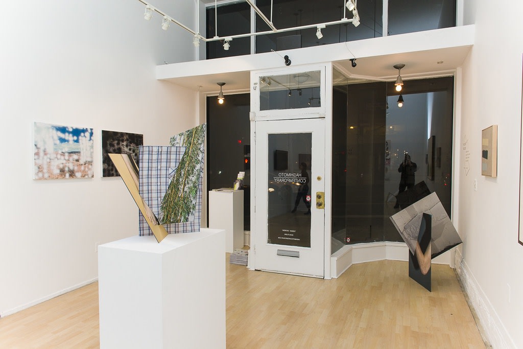 Exhibition installation view featuring abstracted sculptural work in foreground, paintings in background