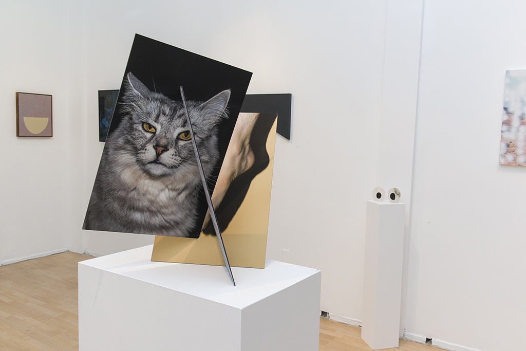 Exhibition installation view featuring abstracted sculptural work in foreground, paintings in background