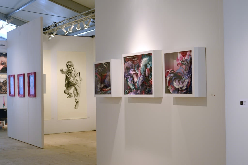 Art fair installation view featuring multimedia work of Crystal Wagner in foreground and a charcoal figurative drawing of Joel Daniel Phillips in background 