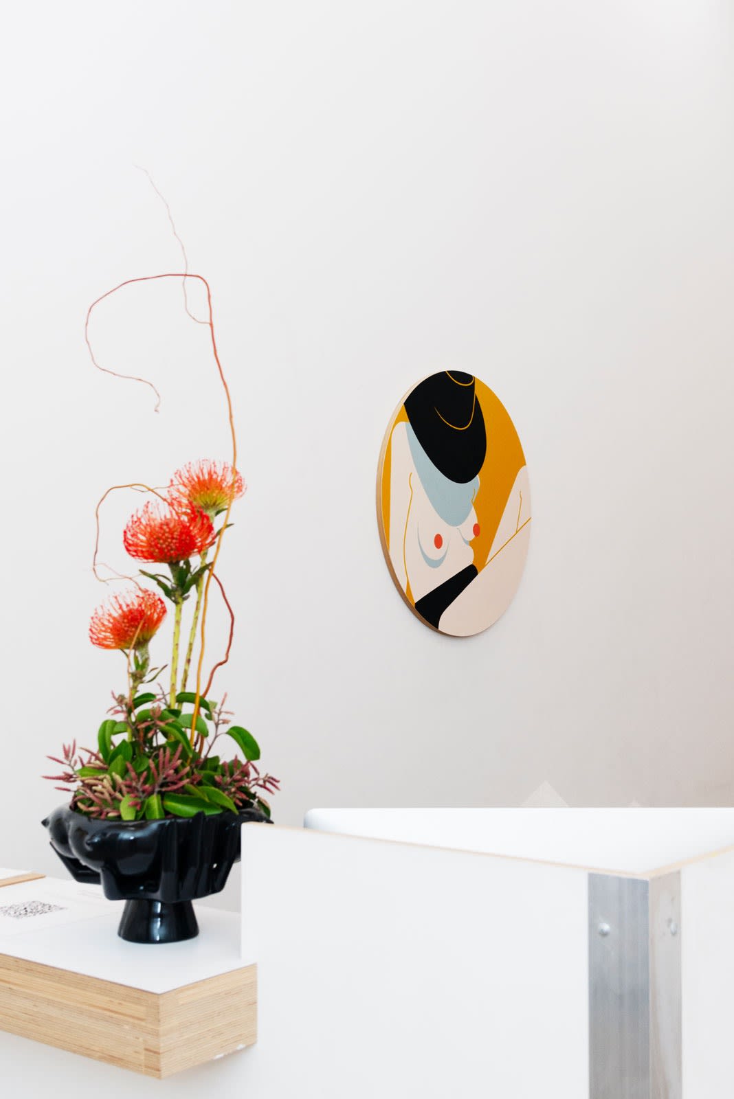 Installation shot of office wall with painting Sun Hat in the background and Bountiful ceramic vase with flowers in the foreground